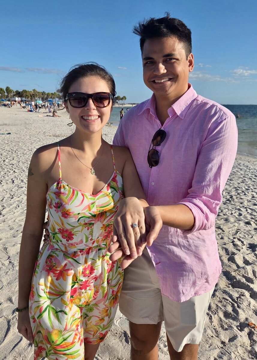 A newly engaged couple showing off the ring at the beach.