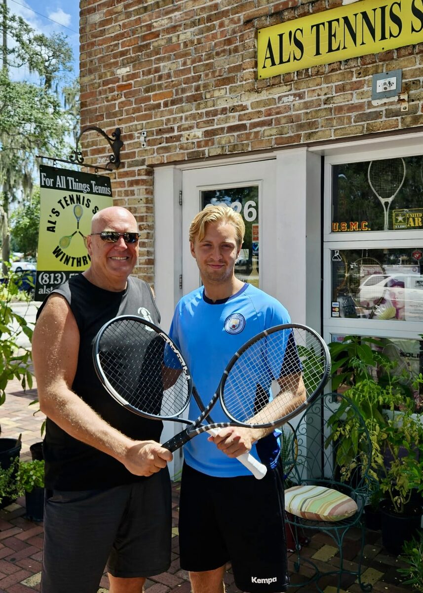 Two players holding racquets outside the front of Al's Tennis Shop.